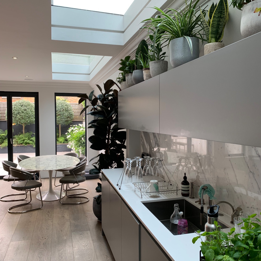 Small contemporary eat-in kitchen in London with a farmhouse sink, flat-panel cabinets, grey cabinets, solid surface benchtops, grey splashback, marble splashback, panelled appliances, medium hardwood floors, with island, beige floor and white benchtop.