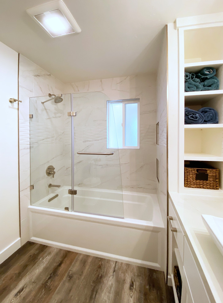 Mid-sized transitional 3/4 black and white tile and porcelain tile vinyl floor, brown floor and single-sink alcove bathtub photo with shaker cabinets, white cabinets, a two-piece toilet, white walls, a vessel sink, quartz countertops, a hinged shower door, gray countertops, a niche and a built-in vanity