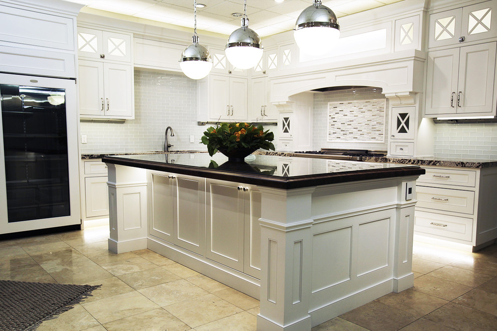 This is an example of a mid-sized beach style l-shaped kitchen in Salt Lake City with recessed-panel cabinets, white cabinets, granite benchtops, white splashback, glass tile splashback, limestone floors, with island and beige floor.