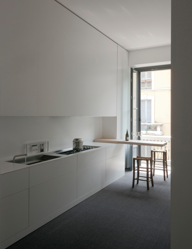 This is an example of a mid-sized modern single-wall separate kitchen in Milan with a single-bowl sink, flat-panel cabinets, white cabinets, quartz benchtops, white splashback, panelled appliances, carpet, a peninsula and grey floor.