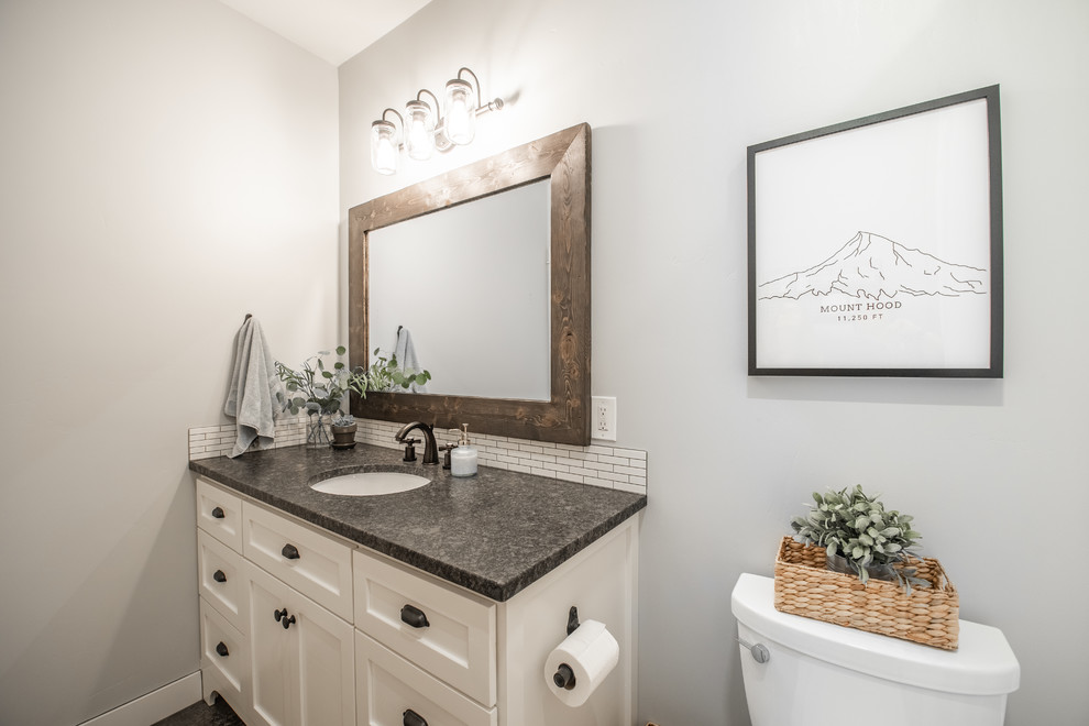 Design ideas for a mid-sized country master bathroom in Seattle with shaker cabinets, white cabinets, an alcove tub, an alcove shower, a two-piece toilet, white tile, porcelain tile, grey walls, concrete floors, an undermount sink, granite benchtops, grey floor, a shower curtain and black benchtops.