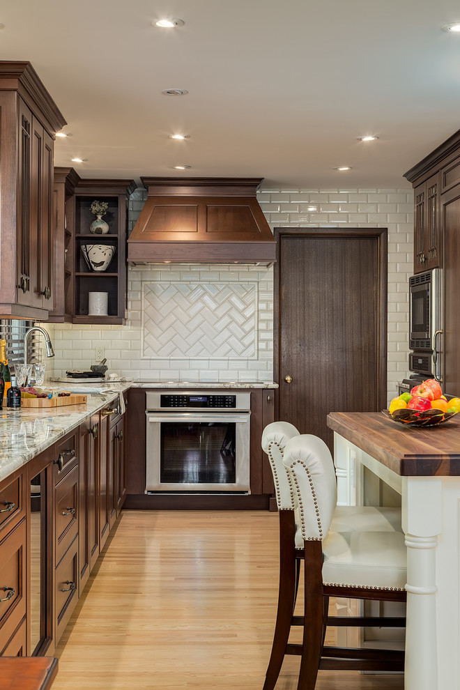 Inspiration for a traditional u-shaped kitchen in Calgary with recessed-panel cabinets, dark wood cabinets, white splashback, subway tile splashback, stainless steel appliances, light hardwood floors and with island.