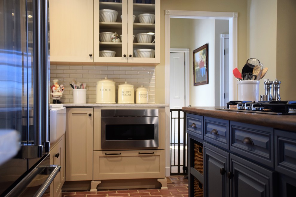 Inspiration for a mid-sized transitional u-shaped brick floor eat-in kitchen remodel with a farmhouse sink, shaker cabinets, white cabinets, quartzite countertops, white backsplash, subway tile backsplash, stainless steel appliances and an island