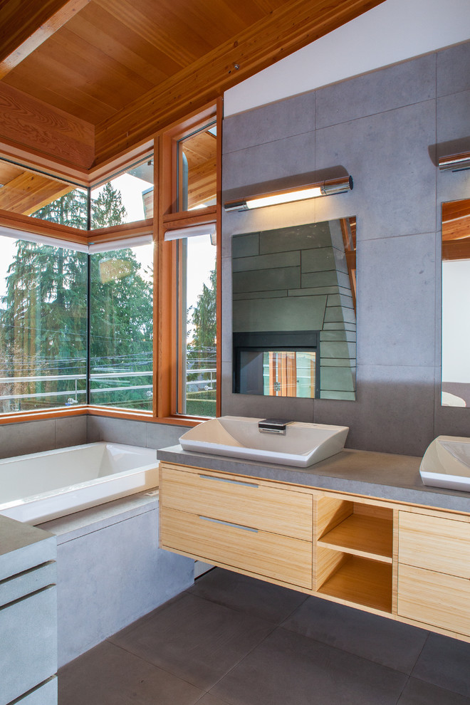 Modern bathroom in Vancouver with a vessel sink, flat-panel cabinets, light wood cabinets, a drop-in tub, gray tile and grey benchtops.