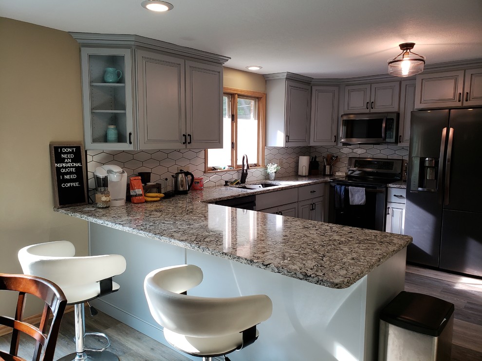 Inspiration for a mid-sized transitional u-shaped medium tone wood floor and brown floor eat-in kitchen remodel with ceramic backsplash, an undermount sink, raised-panel cabinets, gray cabinets, granite countertops, white backsplash, stainless steel appliances, a peninsula and multicolored countertops