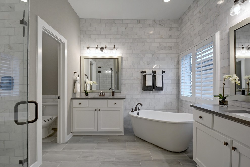Transitional master bathroom in Jacksonville with shaker cabinets, white cabinets, a freestanding tub, an alcove shower, a two-piece toilet, gray tile, white tile, grey walls, an undermount sink, grey floor, a hinged shower door and black benchtops.
