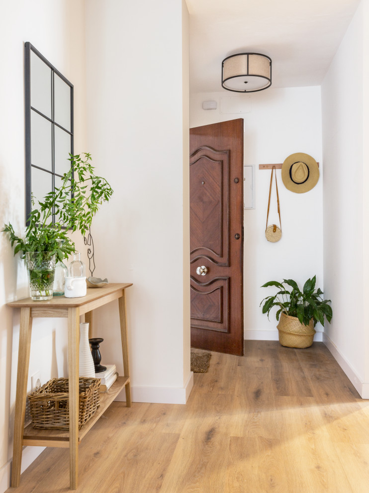 Modelo de hall tradicional renovado pequeño con paredes blancas, suelo laminado, puerta simple, puerta de madera oscura y suelo marrón