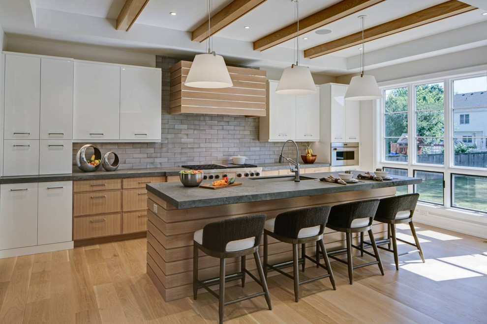 This is an example of a large modern single-wall kitchen in Chicago with an undermount sink, flat-panel cabinets, white cabinets, concrete benchtops, grey splashback, ceramic splashback, stainless steel appliances, light hardwood floors, with island, beige floor, grey benchtop and exposed beam.