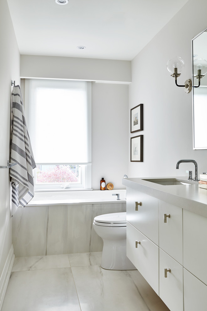 This is an example of a mid-sized contemporary master bathroom in Toronto with flat-panel cabinets, white cabinets, an undermount tub, a one-piece toilet, gray tile, porcelain tile, grey walls, porcelain floors, an undermount sink, engineered quartz benchtops, grey floor and a hinged shower door.