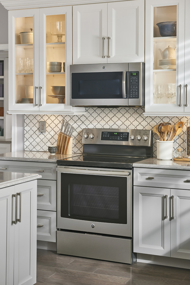 Example of a large classic u-shaped dark wood floor and brown floor enclosed kitchen design in Cincinnati with stainless steel appliances, an island, a double-bowl sink, recessed-panel cabinets, gray cabinets, quartz countertops, white backsplash, porcelain backsplash and gray countertops