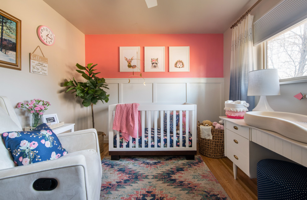 This is an example of a small eclectic nursery for girls in Denver with pink walls, light hardwood flooring and wainscoting.