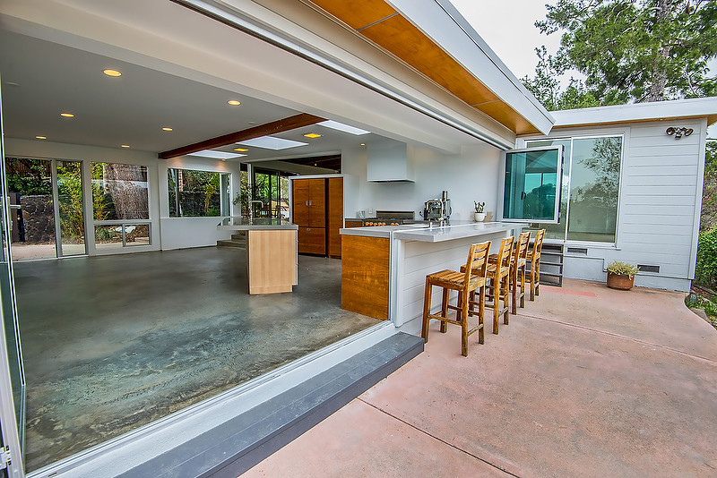 Photo of a mid-sized midcentury l-shaped open plan kitchen in Los Angeles with an undermount sink, flat-panel cabinets, medium wood cabinets, concrete benchtops, stainless steel appliances, concrete floors, with island and grey floor.