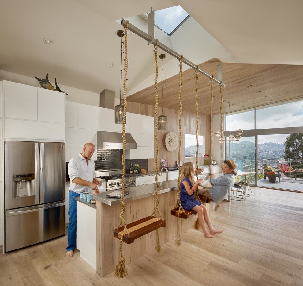 This is an example of a mid-sized contemporary single-wall open plan kitchen in San Francisco with flat-panel cabinets, white cabinets, grey splashback, subway tile splashback, stainless steel appliances, medium hardwood floors, with island and beige floor.