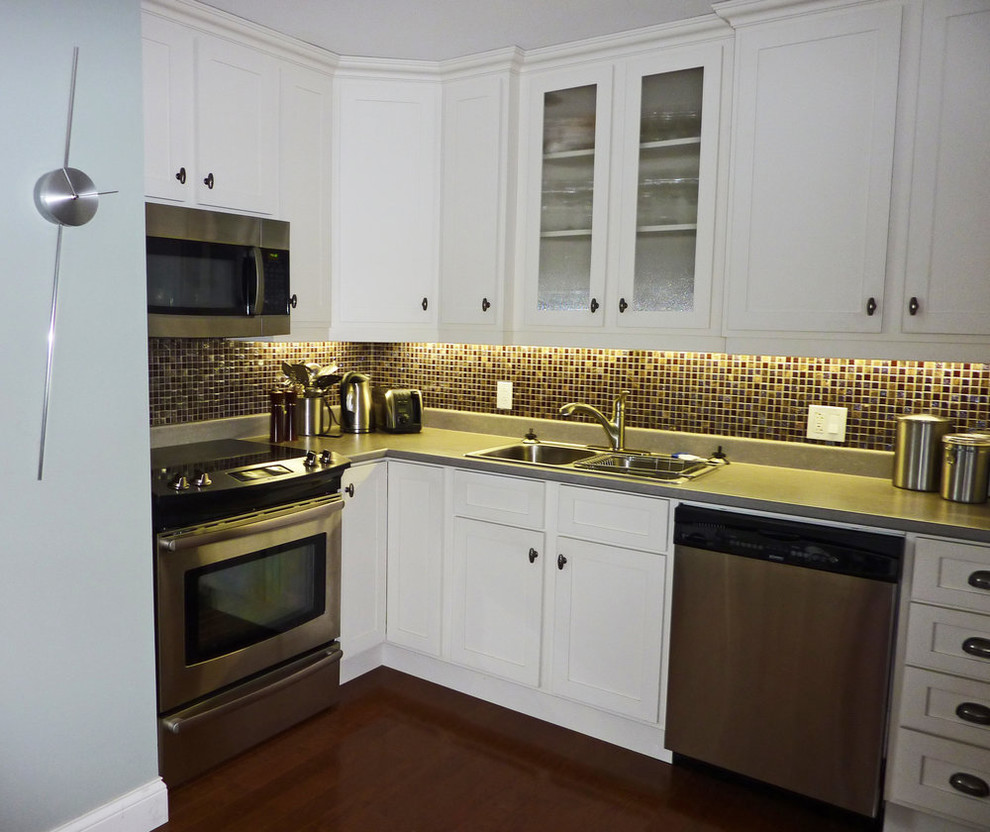 Example of a mid-sized transitional l-shaped medium tone wood floor and brown floor open concept kitchen design with a drop-in sink, shaker cabinets, white cabinets, quartz countertops, multicolored backsplash, mosaic tile backsplash, stainless steel appliances, an island and gray countertops