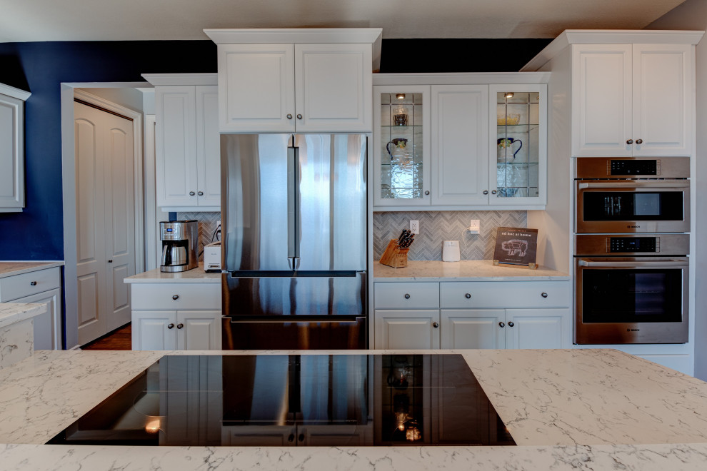 Inredning av ett modernt stort vit vitt kök, med en nedsänkt diskho, luckor med profilerade fronter, granitbänkskiva, blått stänkskydd, stänkskydd i mosaik, rostfria vitvaror, mellanmörkt trägolv, en köksö, brunt golv och vita skåp
