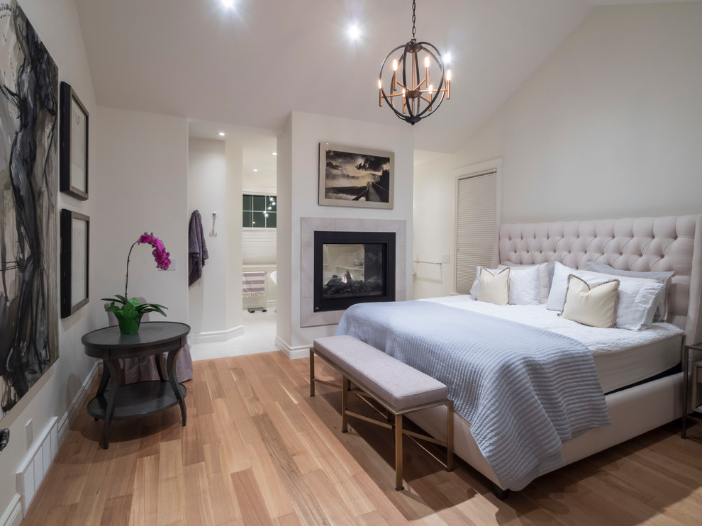 Mid-sized transitional master bedroom in Edmonton with white walls, light hardwood floors, a two-sided fireplace and a tile fireplace surround.