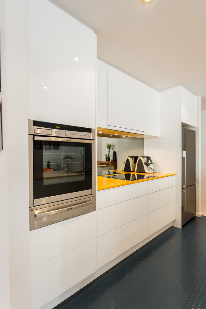 Small contemporary galley open plan kitchen in Perth with an undermount sink, flat-panel cabinets, white cabinets, quartz benchtops, glass sheet splashback and stainless steel appliances.