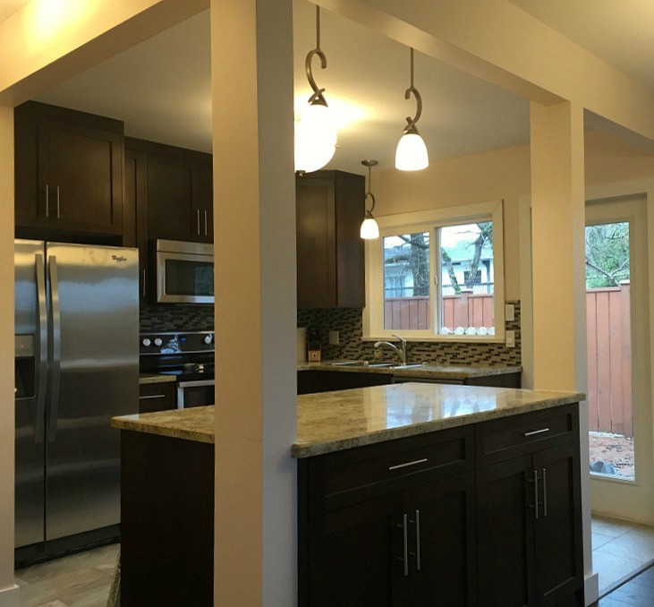 This is an example of a small traditional l-shaped eat-in kitchen in Vancouver with a double-bowl sink, flat-panel cabinets, brown cabinets, laminate benchtops, glass tile splashback, stainless steel appliances, dark hardwood floors and with island.