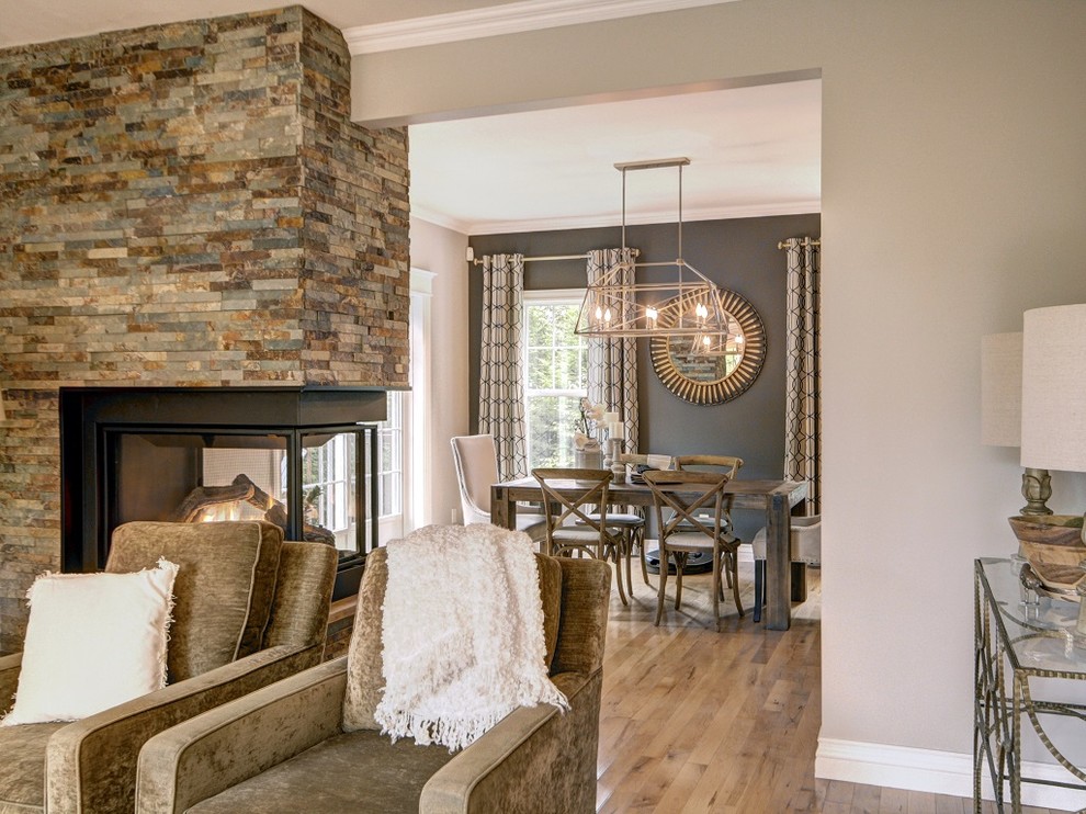 This is an example of a mid-sized transitional separate dining room in Other with grey walls, light hardwood floors, a two-sided fireplace, a stone fireplace surround and brown floor.
