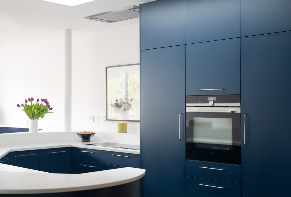 Inspiration for a mid-sized eclectic u-shaped open plan kitchen in London with a double-bowl sink, flat-panel cabinets, blue cabinets, solid surface benchtops, panelled appliances, concrete floors and a peninsula.