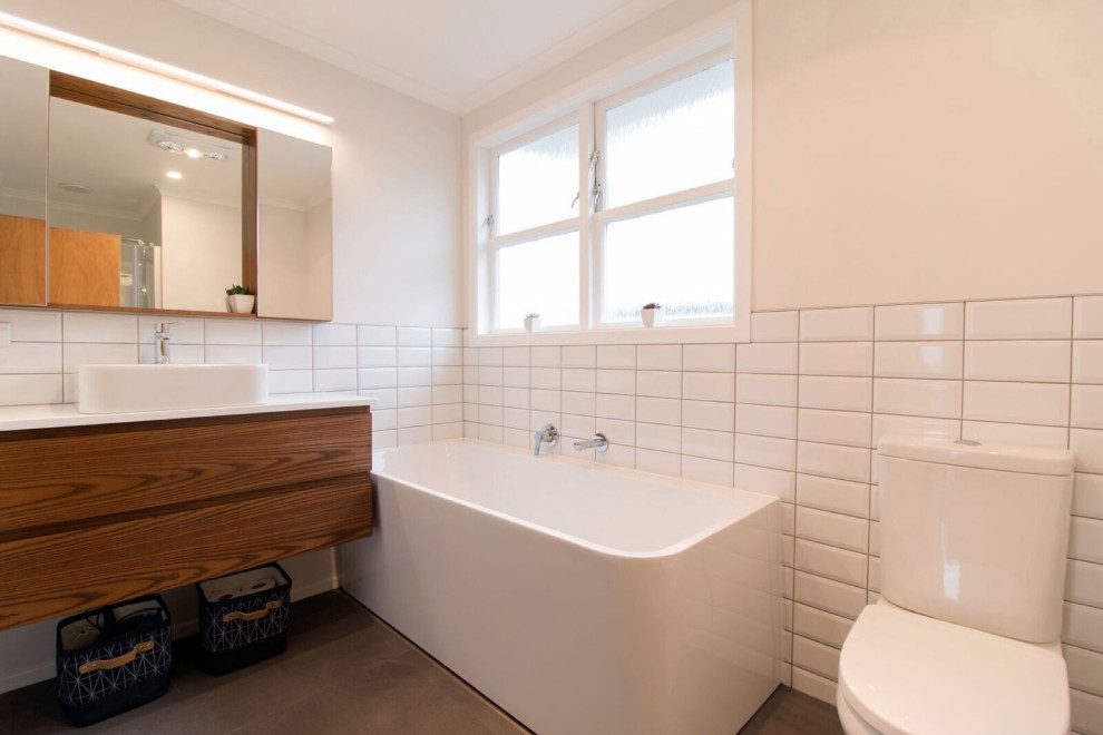 Photo of a medium sized retro ensuite bathroom in Sydney with freestanding cabinets, dark wood cabinets, a corner bath, white tiles, porcelain tiles, brown floors, white worktops, a single sink and a floating vanity unit.