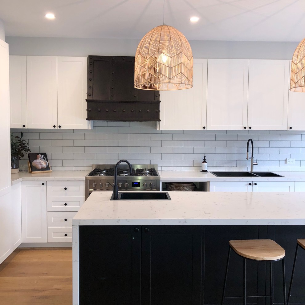 Inspiration for a transitional l-shaped kitchen in Melbourne with a drop-in sink, shaker cabinets, white cabinets, white splashback, subway tile splashback, medium hardwood floors, with island, beige floor and white benchtop.