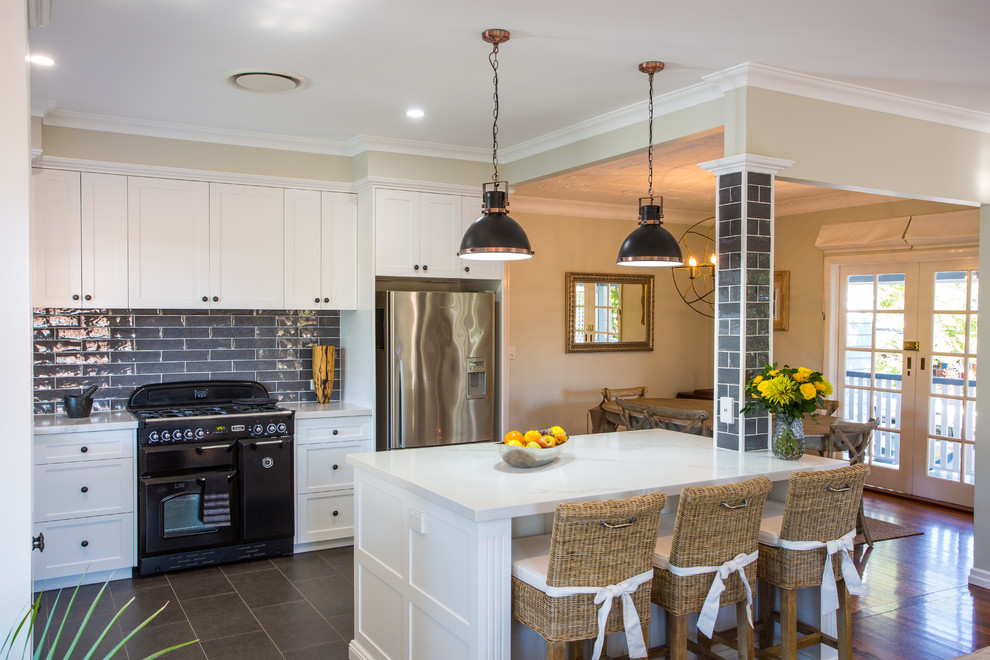 Large traditional l-shaped open plan kitchen in Brisbane with an undermount sink, shaker cabinets, white cabinets, quartz benchtops, grey splashback, black appliances, ceramic floors, with island and grey floor.