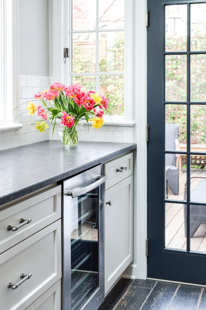 Large transitional l-shaped porcelain tile enclosed kitchen photo in New York with an undermount sink, flat-panel cabinets, white cabinets, granite countertops, white backsplash, ceramic backsplash, stainless steel appliances and an island