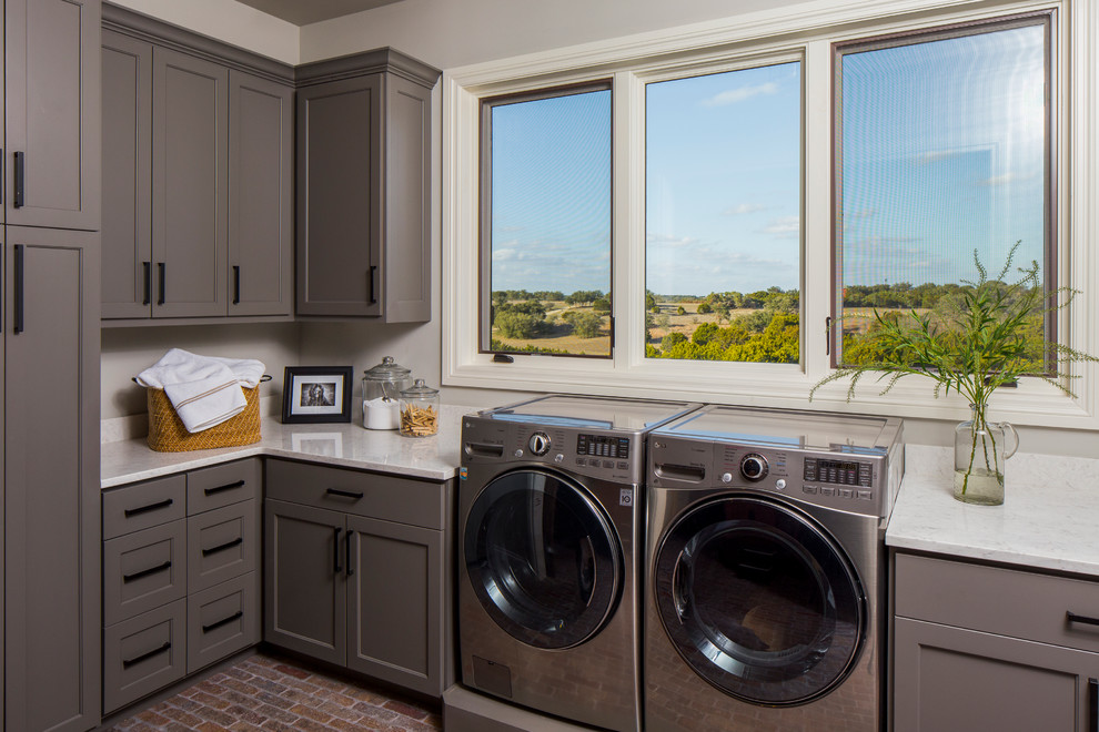 Inspiration for a mid-sized traditional dedicated laundry room in Austin with shaker cabinets, grey cabinets, solid surface benchtops, grey walls, brick floors, a side-by-side washer and dryer and brown floor.