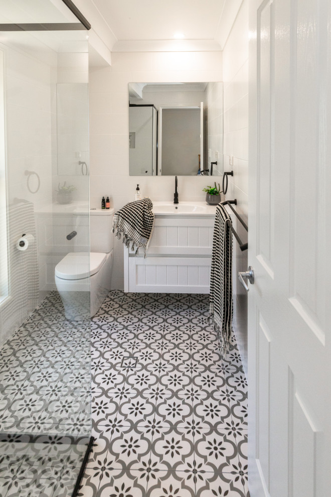 This is an example of a small modern bathroom in Other with shaker cabinets, white cabinets, a corner shower, a two-piece toilet, white tile, ceramic tile, white walls, cement tiles, an integrated sink, solid surface benchtops, a hinged shower door and white benchtops.