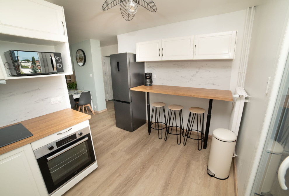 Photo of a small transitional single-wall open plan kitchen in Other with an undermount sink, recessed-panel cabinets, beige cabinets, wood benchtops, white splashback, stone slab splashback, black appliances, laminate floors, brown floor and brown benchtop.
