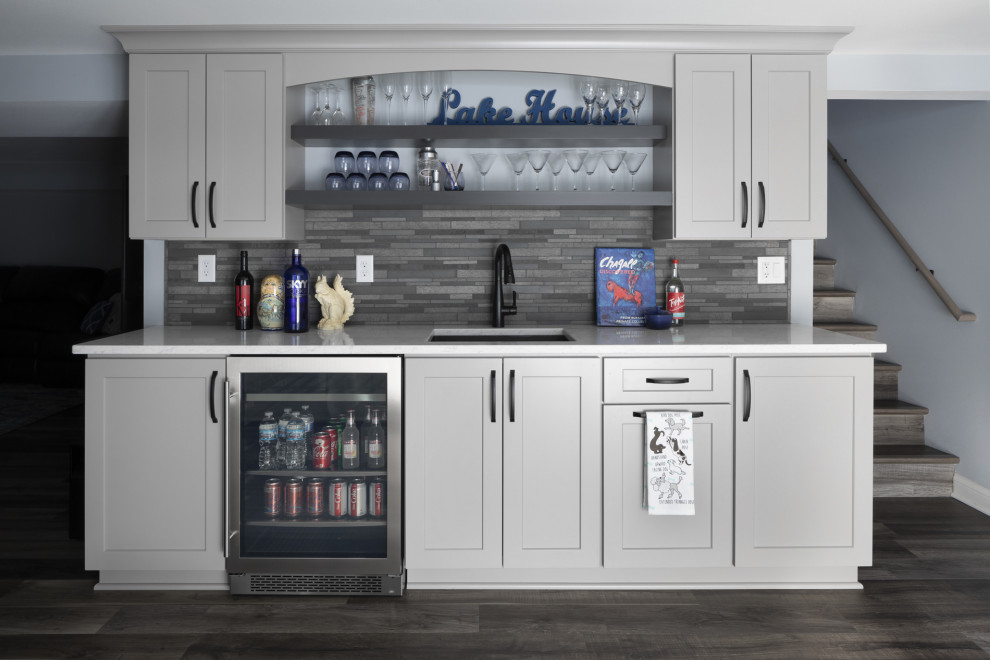 Inspiration for a mid-sized transitional single-wall wet bar in Milwaukee with an undermount sink, shaker cabinets, grey cabinets, quartz benchtops, grey splashback, stone tile splashback, vinyl floors, grey floor and grey benchtop.