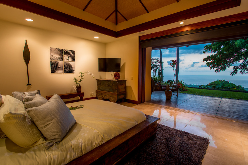 This is an example of a mid-sized tropical master bedroom in Hawaii with beige walls and limestone floors.