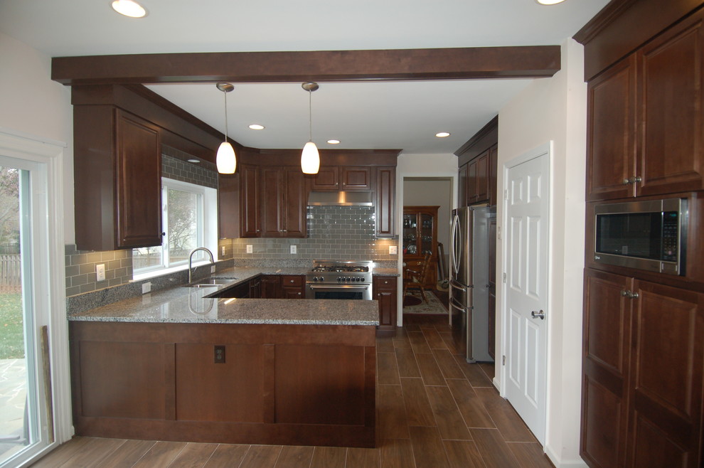 Photo of a mid-sized transitional u-shaped eat-in kitchen in DC Metro with an undermount sink, shaker cabinets, dark wood cabinets, granite benchtops, grey splashback, glass tile splashback, stainless steel appliances, plywood floors and a peninsula.