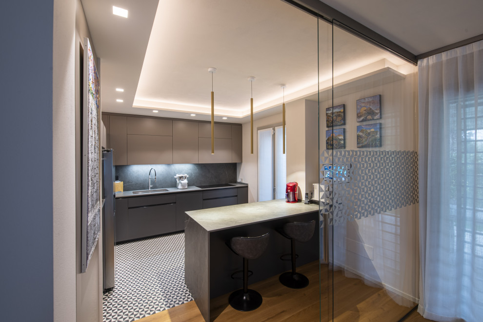 This is an example of a mid-sized l-shaped open plan kitchen in Florence with an undermount sink, flat-panel cabinets, grey cabinets, quartz benchtops, grey splashback, porcelain splashback, stainless steel appliances, porcelain floors, a peninsula, multi-coloured floor, grey benchtop and recessed.