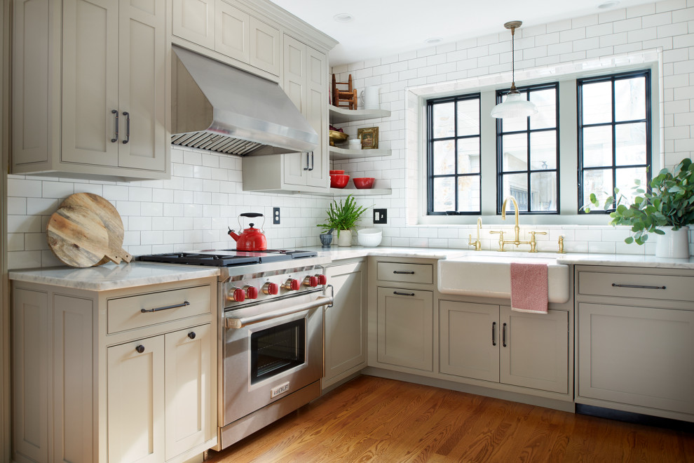 This is an example of a mid-sized transitional u-shaped open plan kitchen in Philadelphia with a farmhouse sink, beaded inset cabinets, beige cabinets, marble benchtops, white splashback, subway tile splashback, panelled appliances, medium hardwood floors, a peninsula, orange floor and white benchtop.