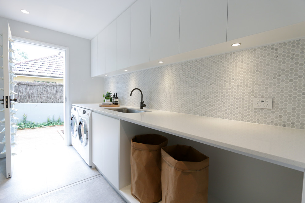 Modern dedicated laundry room in Sydney with an undermount sink, flat-panel cabinets, white cabinets, a side-by-side washer and dryer, grey floor and white benchtop.