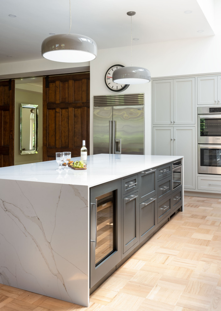 Example of a large transitional light wood floor eat-in kitchen design with an undermount sink, recessed-panel cabinets, gray cabinets, quartz countertops, white backsplash, quartz backsplash, stainless steel appliances, an island and white countertops