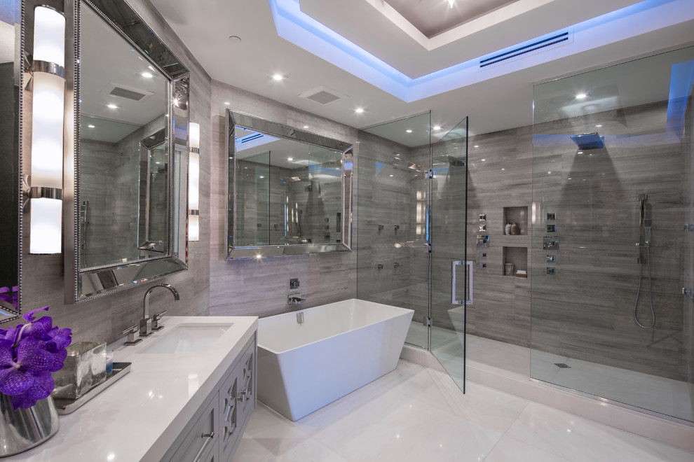 Large contemporary master bathroom in Miami with recessed-panel cabinets, grey cabinets, a freestanding tub, a double shower, gray tile, porcelain tile, white walls, porcelain floors, an undermount sink, engineered quartz benchtops, white floor and a hinged shower door.