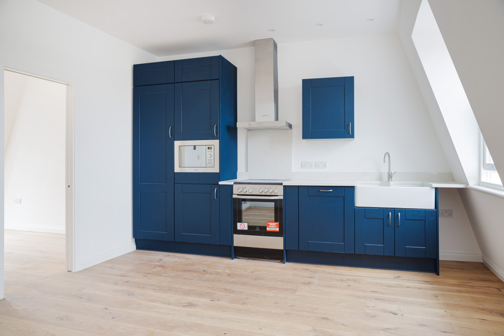 Inspiration for a small contemporary single-wall eat-in kitchen in London with a farmhouse sink, shaker cabinets, blue cabinets, marble benchtops, white splashback, marble splashback, stainless steel appliances, laminate floors, no island, brown floor and white benchtop.