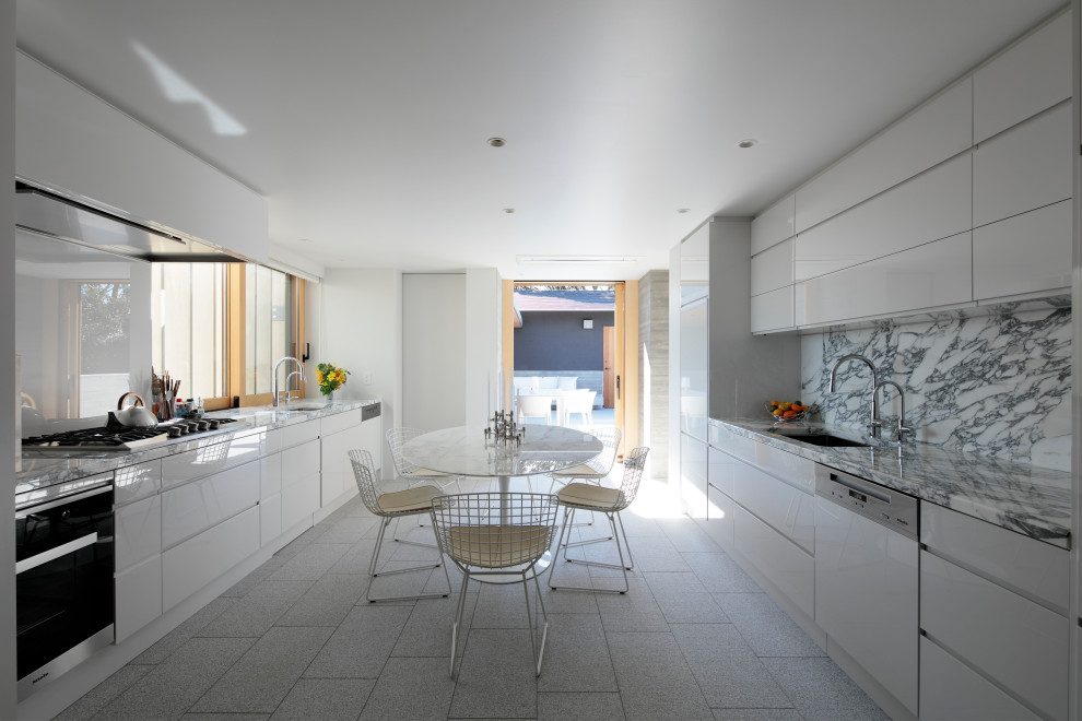 Photo of a contemporary galley eat-in kitchen in Other with an undermount sink, flat-panel cabinets, white cabinets, grey splashback, white appliances, no island, grey floor and grey benchtop.