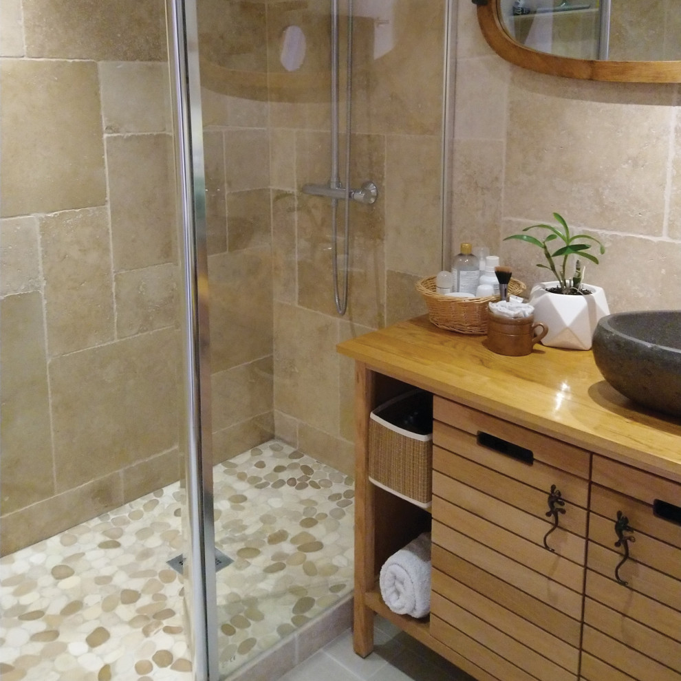 Inspiration för ett litet tropiskt badrum med dusch, med skåp i ljust trä, en kantlös dusch, beige kakel, travertinkakel, beige väggar, ett fristående handfat, träbänkskiva, grått golv och med dusch som är öppen