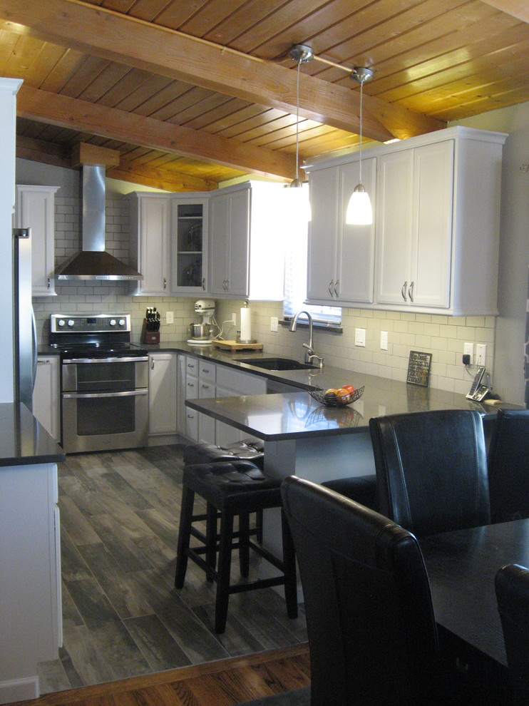 Inspiration for a mid-sized transitional u-shaped dark wood floor and brown floor kitchen remodel in Denver with an undermount sink, recessed-panel cabinets, white cabinets, quartz countertops, white backsplash, subway tile backsplash, stainless steel appliances, a peninsula and gray countertops