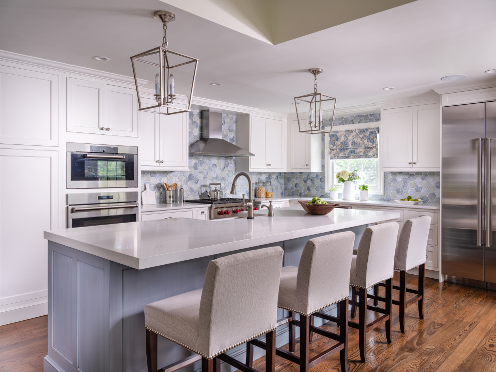 Transitional l-shaped eat-in kitchen in New York with a farmhouse sink, shaker cabinets, white cabinets, quartz benchtops, blue splashback, porcelain splashback, stainless steel appliances, medium hardwood floors, with island, brown floor, white benchtop and recessed.