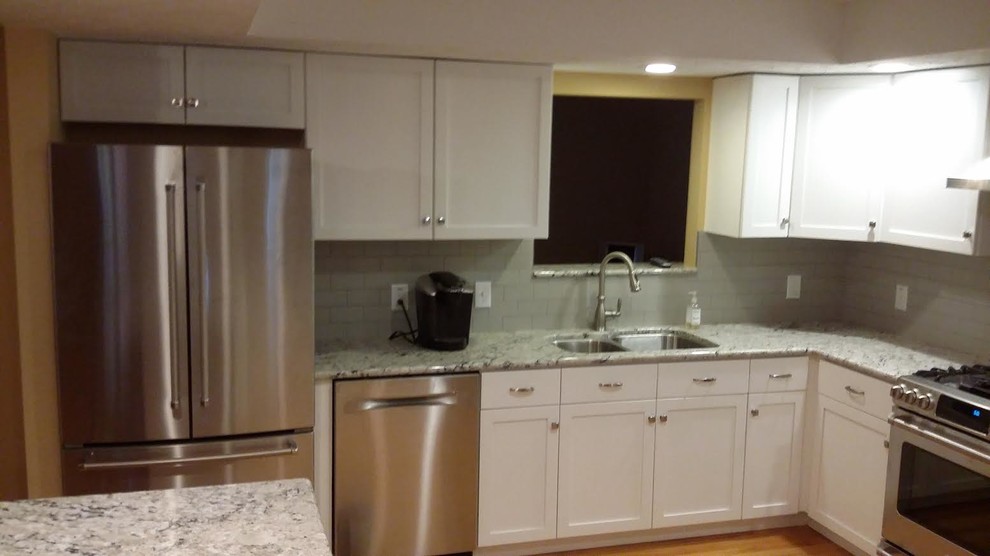 Mid-sized transitional l-shaped medium tone wood floor and brown floor open concept kitchen photo with a double-bowl sink, shaker cabinets, white cabinets, granite countertops, gray backsplash, subway tile backsplash, stainless steel appliances and an island