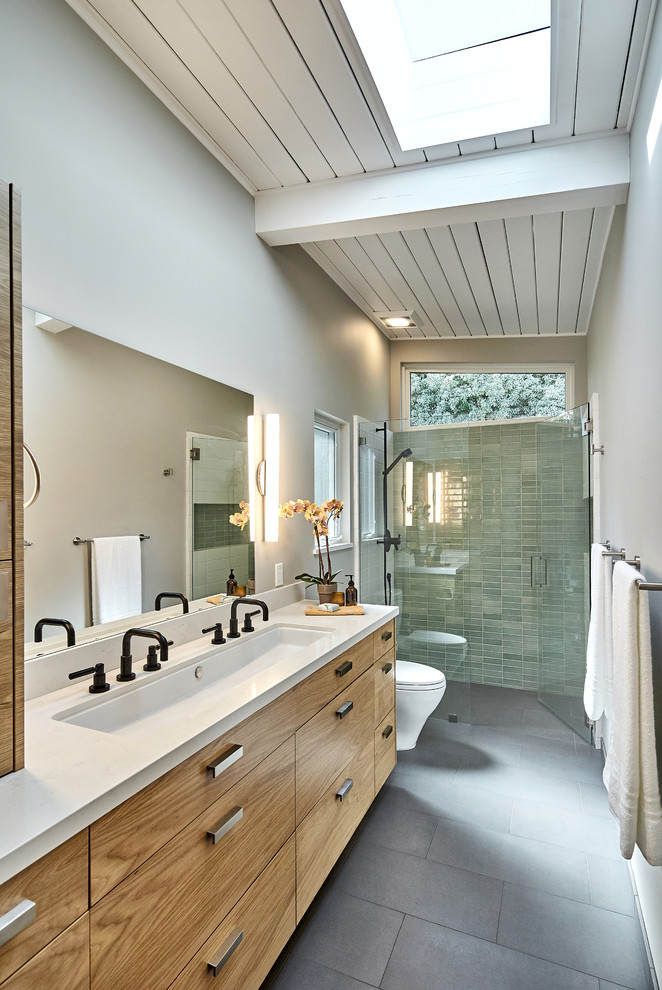 Inspiration for a mid-sized contemporary master bathroom in San Francisco with flat-panel cabinets, medium wood cabinets, a curbless shower, a one-piece toilet, green tile, ceramic tile, grey walls, ceramic floors, quartzite benchtops, grey floor, a hinged shower door, a trough sink, white benchtops and exposed beam.