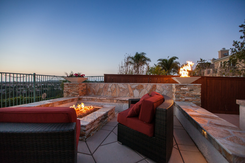 This is an example of a beach style backyard patio in San Diego with a fire feature and natural stone pavers.