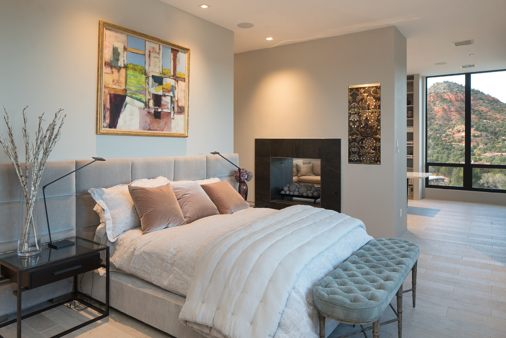 This is an example of a large contemporary master bedroom in Phoenix with grey walls, beige floor, light hardwood floors and a two-sided fireplace.