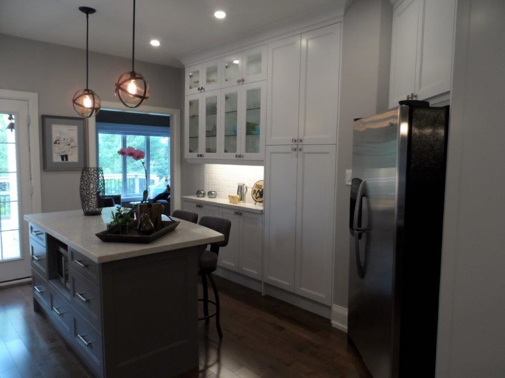 This is an example of a large transitional galley separate kitchen in Toronto with an undermount sink, recessed-panel cabinets, white cabinets, marble benchtops, white splashback, subway tile splashback, stainless steel appliances, dark hardwood floors, with island and brown floor.