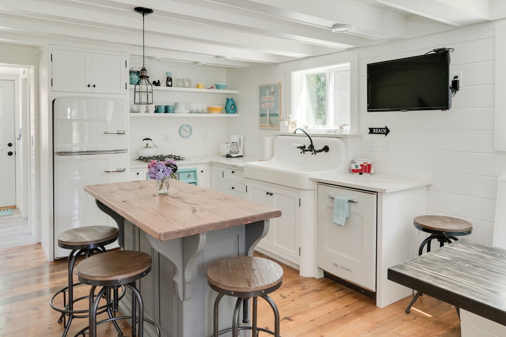 Inspiration for a beach style l-shaped kitchen in Grand Rapids with shaker cabinets, white cabinets, wood benchtops, white appliances, light hardwood floors and with island.